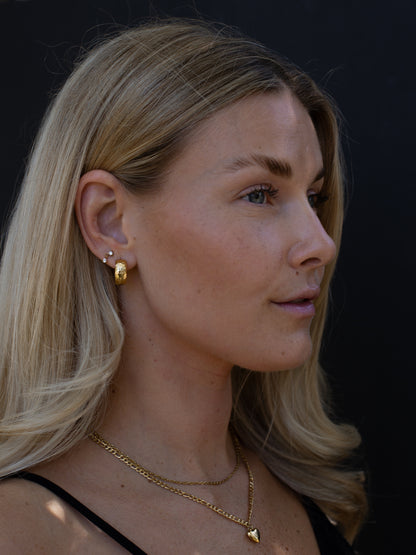 Woman wearing gold earrings and necklace against a dark background